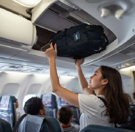 A passenger places a carry-on bag into the overhead bin inside an airplane cabin.
